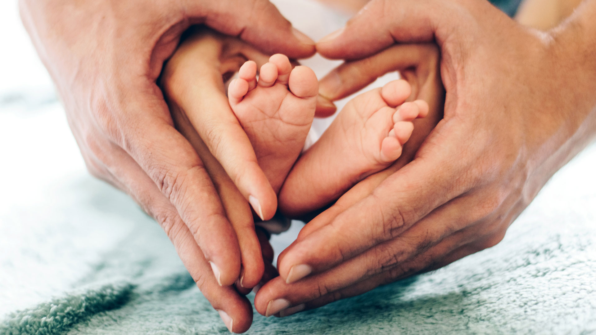 Father and mother holding their child's feet, forming a heart shape with their hands.