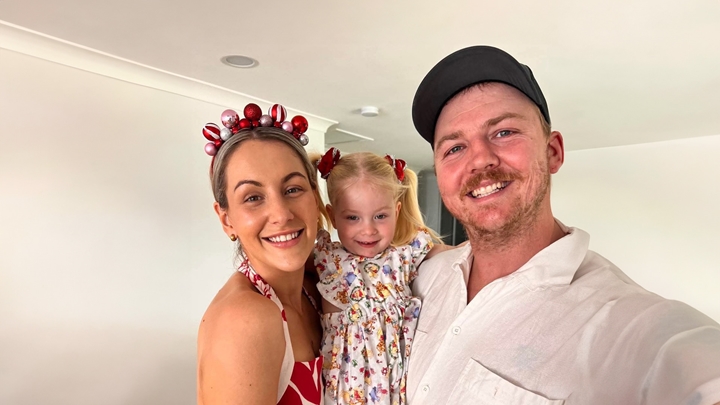 Brandon and Jasmine smiling at the camera while holding their young daughter in a family selfie.