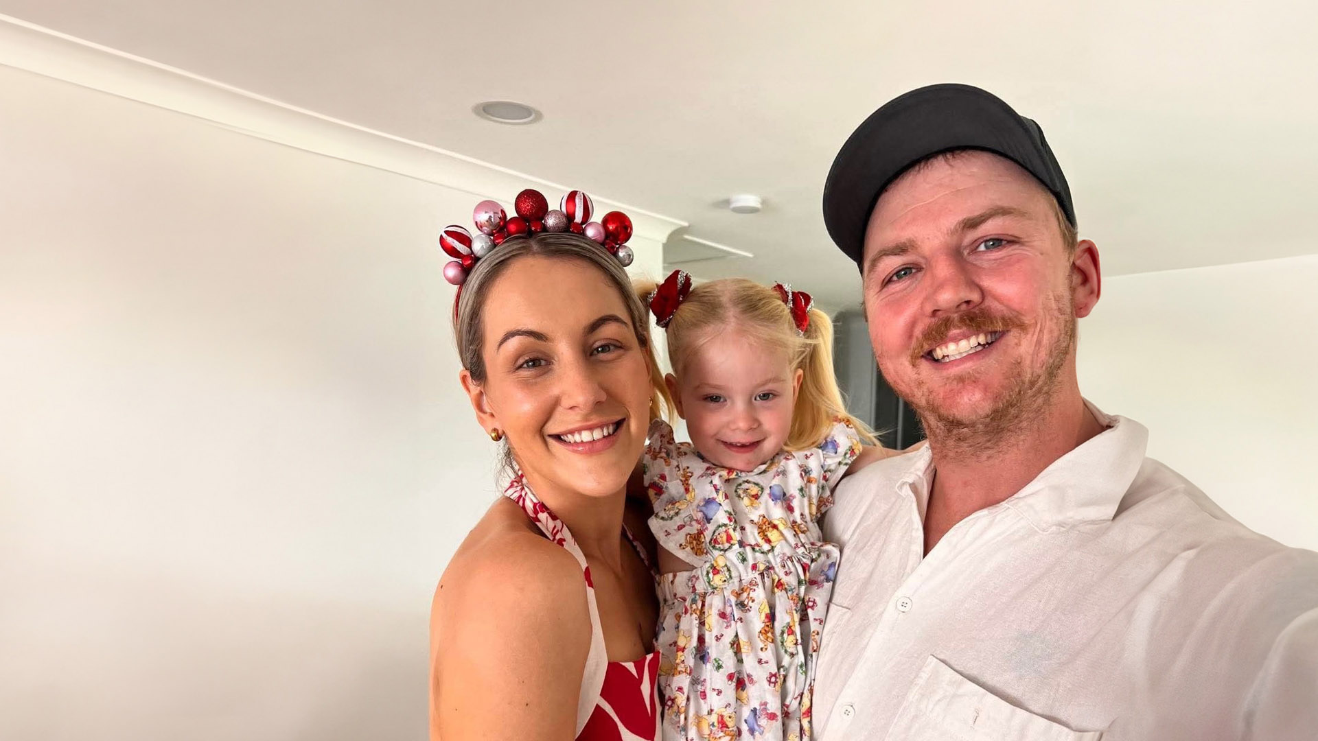 Brandon and Jasmine smiling at the camera while holding their young daughter in a family selfie.