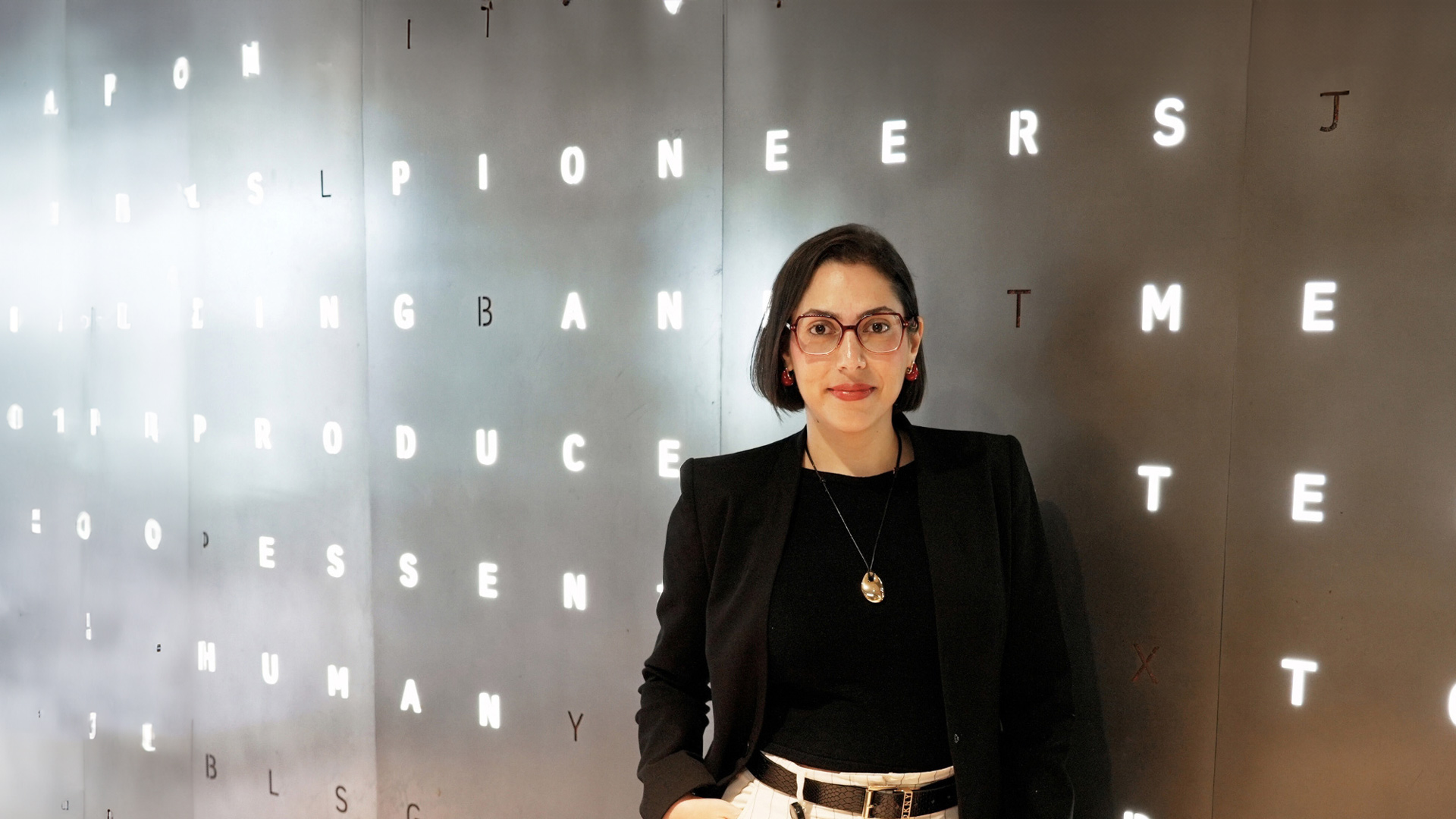 Fernanda, standing against a dark wall featuring illuminated letters arranged in a scattered pattern.