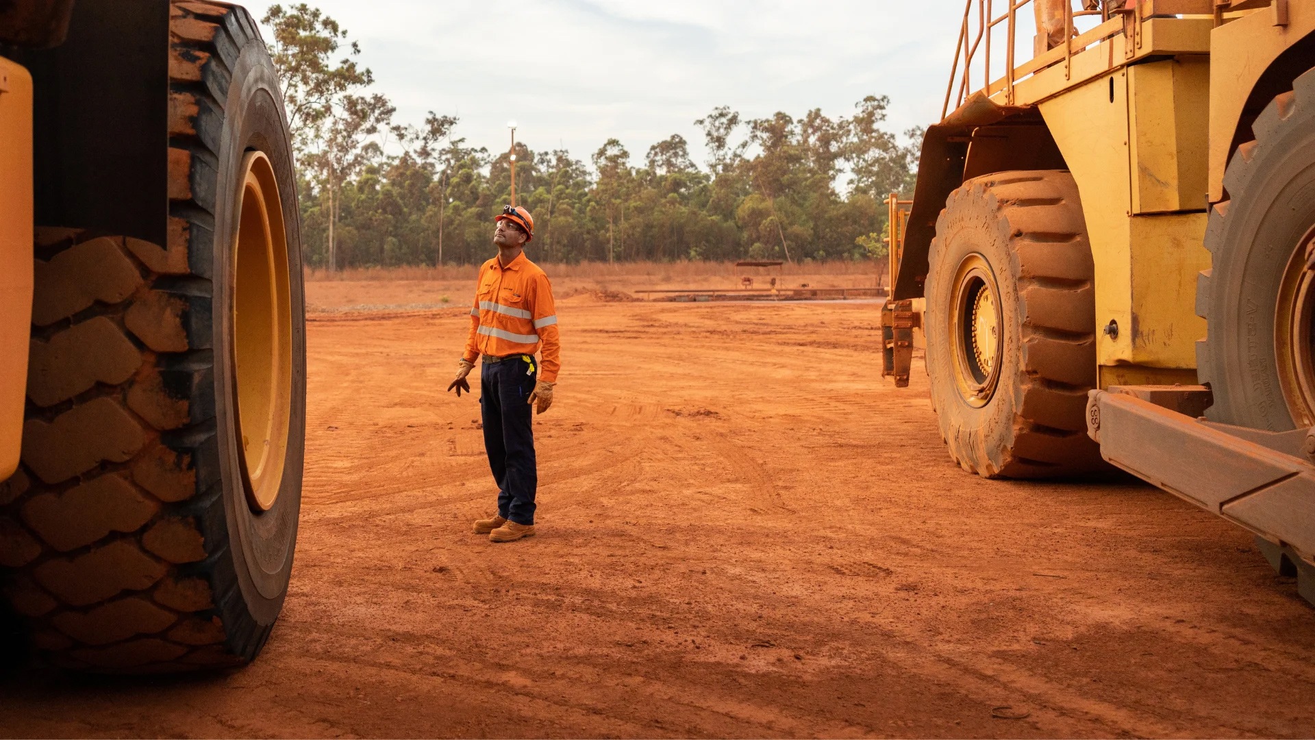 A large truck tyres being looked at by a worker wearing safety gears.