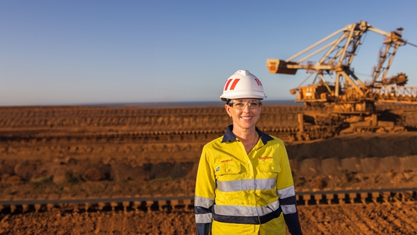 Portrait shot of Michelle, General Manager of Dampier Port Operations posing in front of large crane wearing a safety shirt and helmet. 