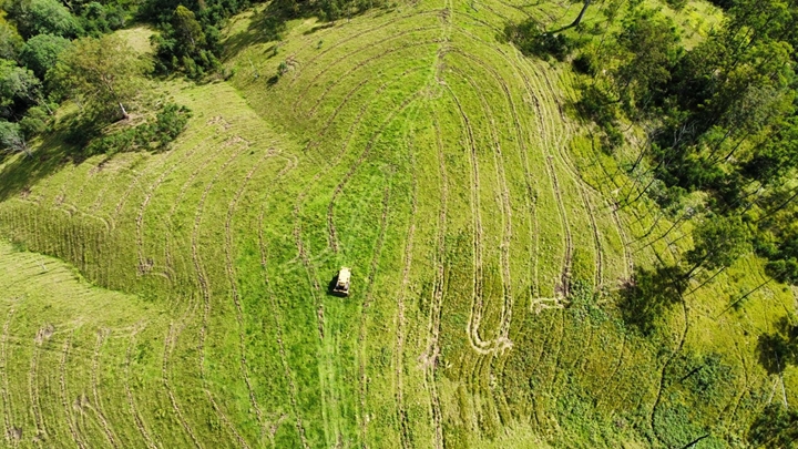 Aerial view of green farmland with curved mowing patterns and a small tractor working in the center.