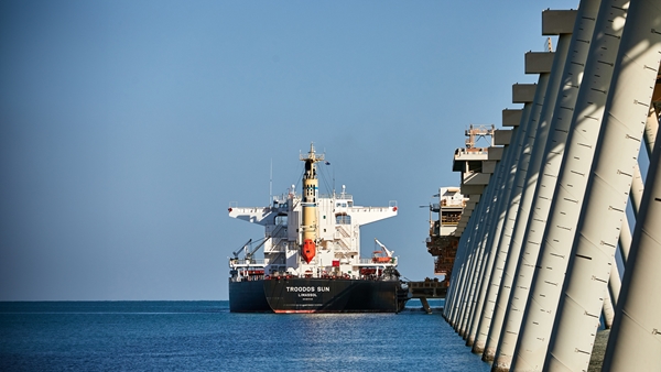 Cargo ship arriving at a port beside a pier under a clear blue sky.