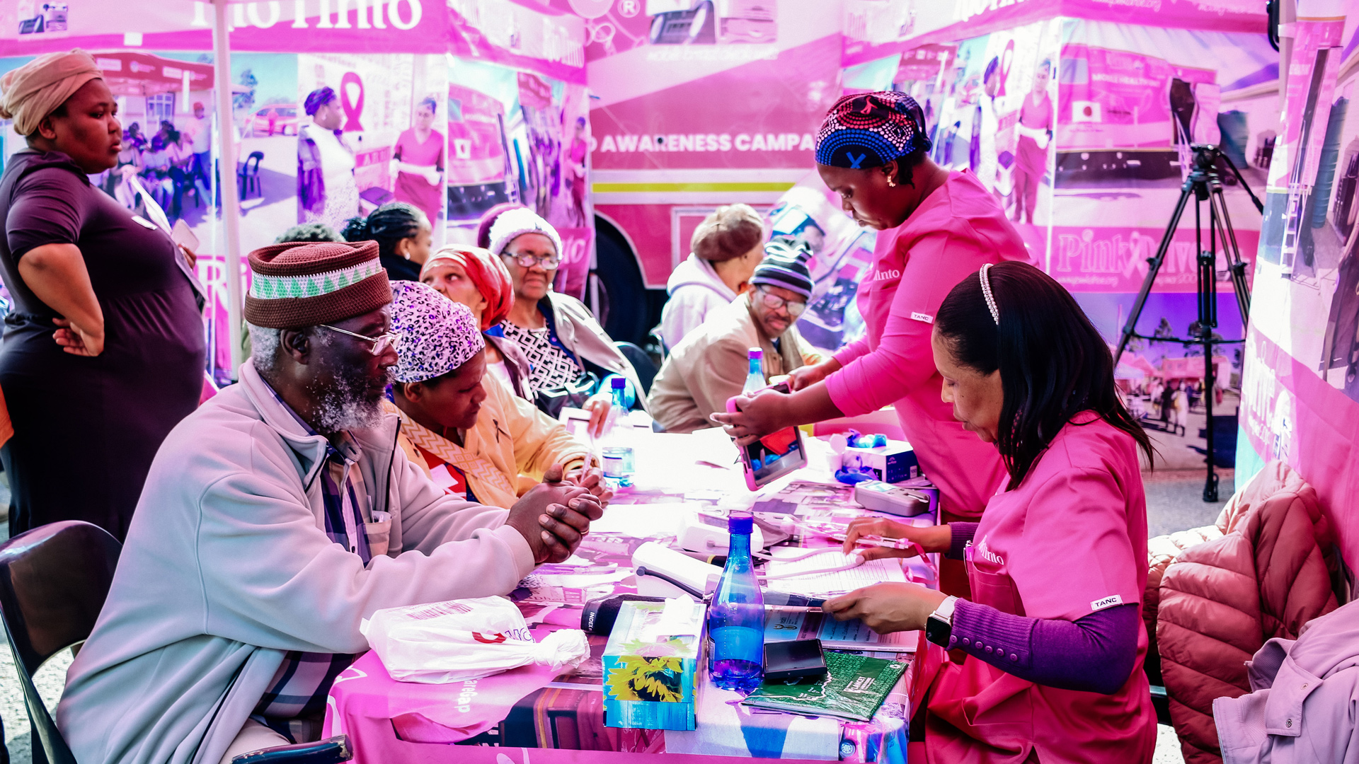 A community health outreach tent decorated in pink hosts an educational session in a rural South African setting.