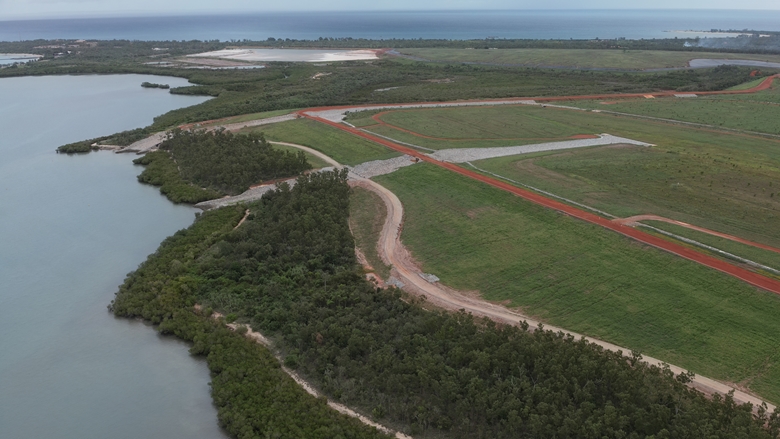 Aerial view of a coastal landscape showing green vegetation, waterways, and red earth access roads.