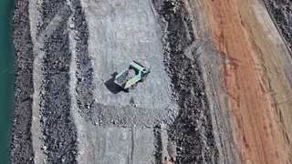 Aerial view of a haul truck transporting crushed rock through a quarry or mining site, surrounded by stockpiles of excavated material and earthworks.