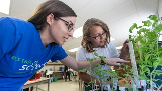Image of a teacher guiding her young student to measure the height of plants on a table.