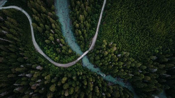 Vue aérienne d’une route sinueuse traversant une rivière turquoise au cœur d’une forêt dense et verdoyante.