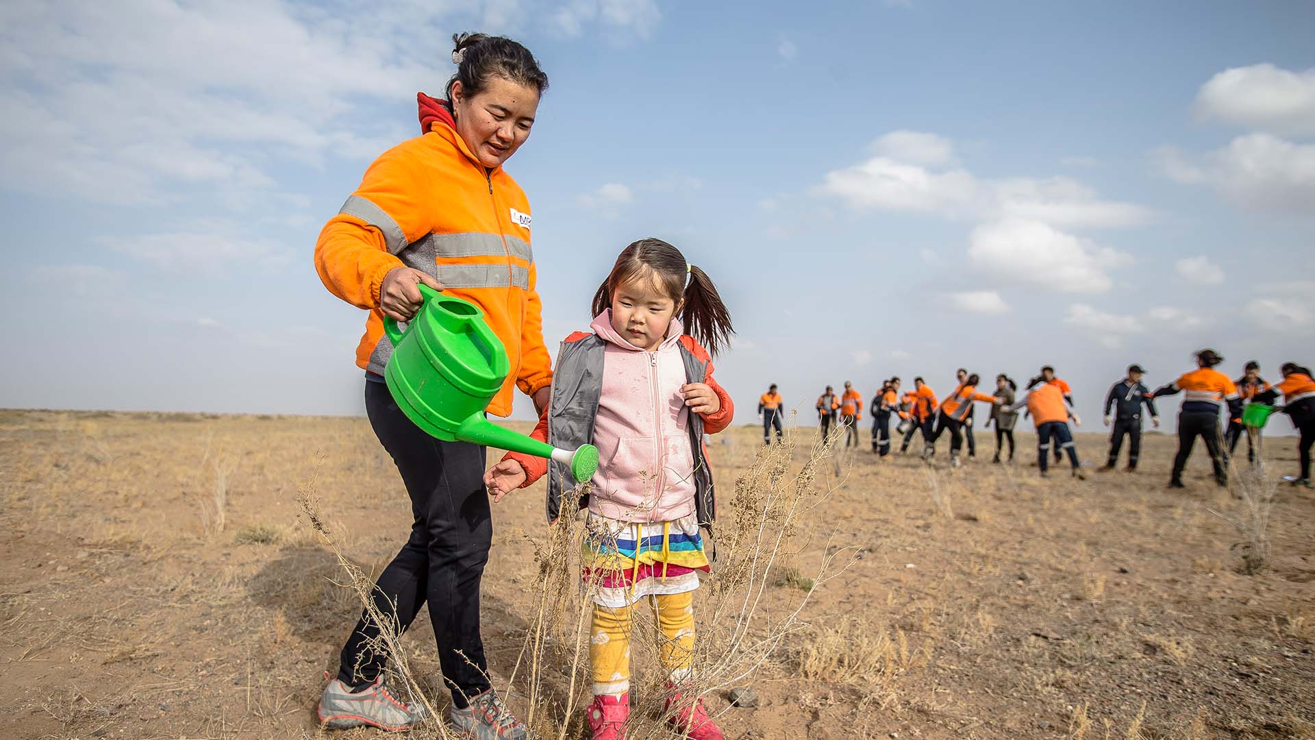 An OT employee and her daughter water trees at a tree planting event, Khanbogd soum, Umnugobi aimag